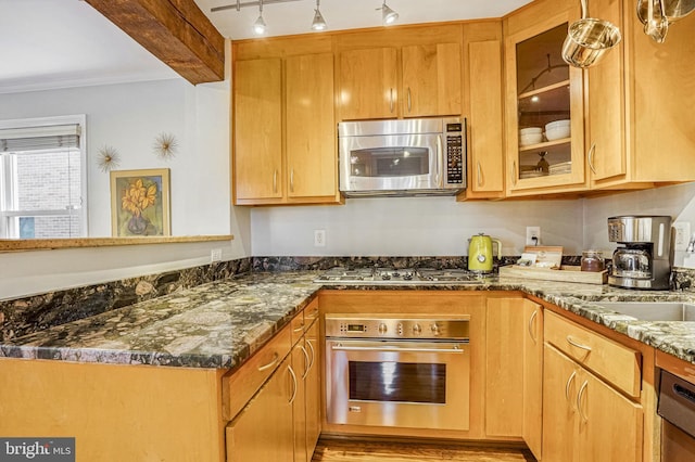 kitchen featuring crown molding, beam ceiling, stainless steel appliances, track lighting, and dark stone counters