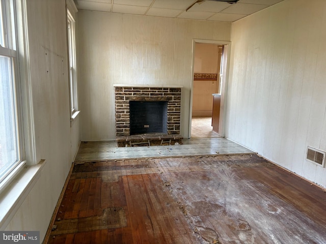 unfurnished living room featuring a drop ceiling, hardwood / wood-style floors, a fireplace, and wood walls