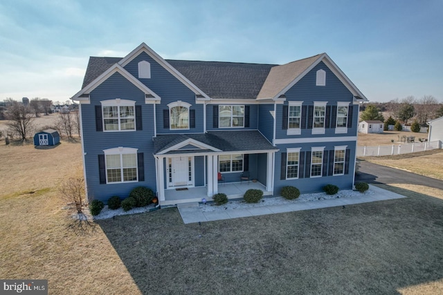 view of front of home featuring a front yard, covered porch, and a shed