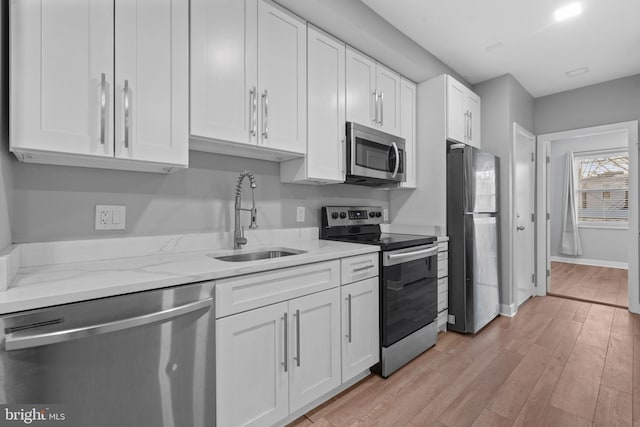 kitchen with sink, appliances with stainless steel finishes, light stone countertops, white cabinets, and light wood-type flooring