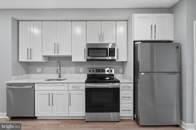 kitchen featuring sink, light hardwood / wood-style flooring, white cabinetry, stainless steel appliances, and light stone counters