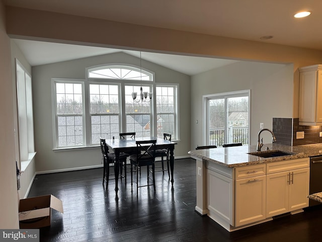 kitchen featuring pendant lighting, lofted ceiling, light stone countertops, and sink