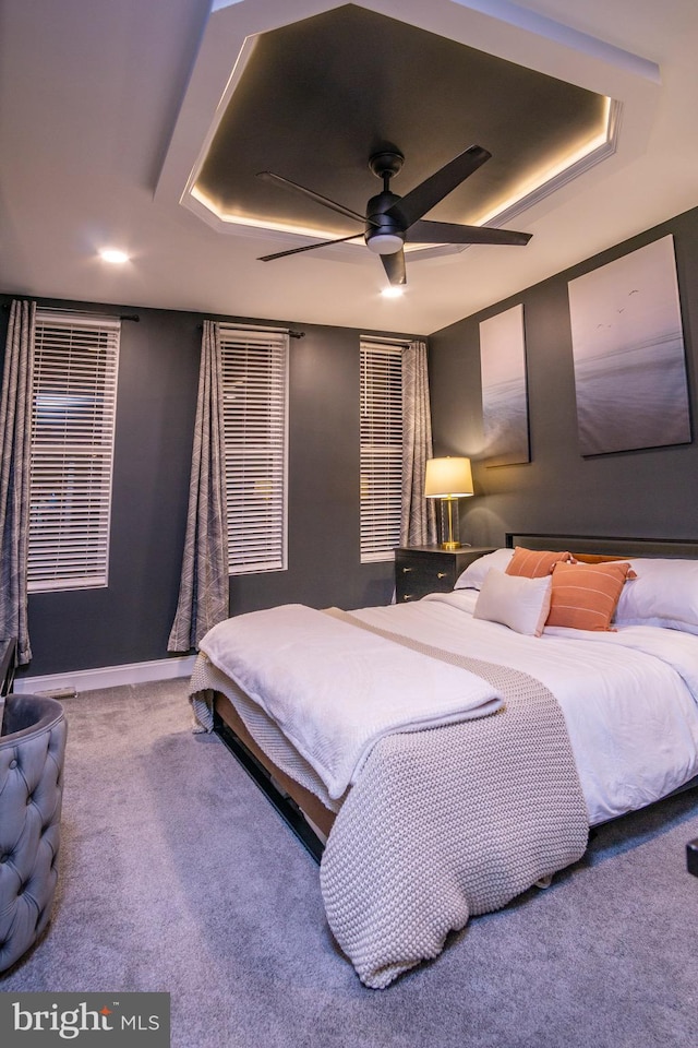 carpeted bedroom with a raised ceiling and ceiling fan