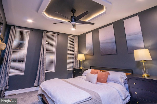 carpeted bedroom featuring ceiling fan and a tray ceiling