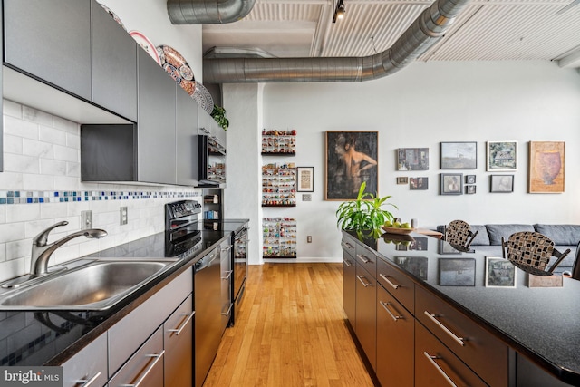 kitchen featuring sink, stainless steel appliances, tasteful backsplash, dark stone counters, and light wood-type flooring