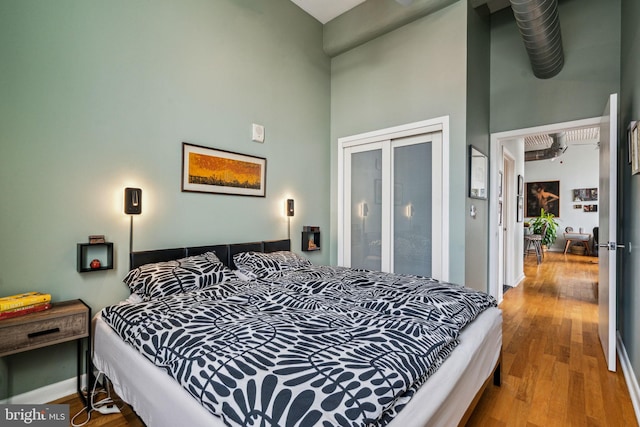 bedroom with hardwood / wood-style flooring, a towering ceiling, and a closet