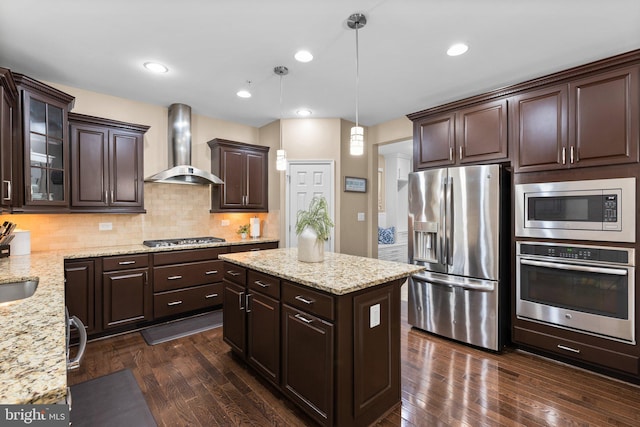 kitchen with appliances with stainless steel finishes, decorative light fixtures, dark brown cabinets, and wall chimney exhaust hood