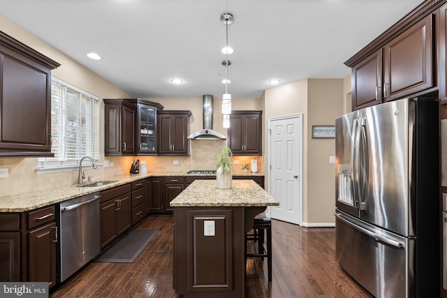 kitchen featuring pendant lighting, wall chimney range hood, appliances with stainless steel finishes, dark brown cabinets, and a kitchen island