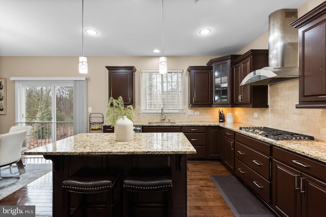 kitchen featuring pendant lighting, sink, a breakfast bar area, stainless steel gas cooktop, and wall chimney exhaust hood