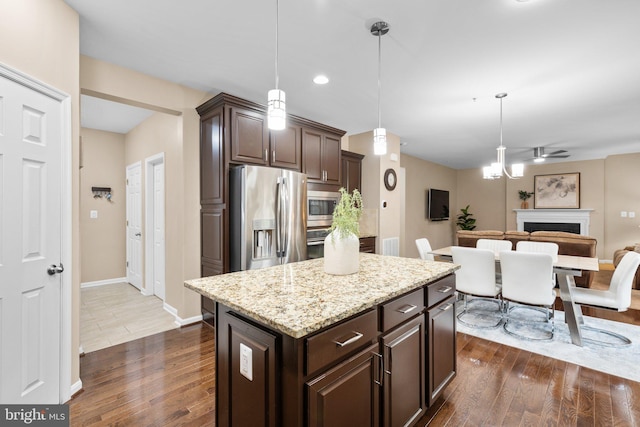 kitchen with dark brown cabinetry, a center island, hanging light fixtures, appliances with stainless steel finishes, and dark hardwood / wood-style flooring