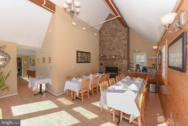 dining room featuring light wood finished floors, a stone fireplace, high vaulted ceiling, beamed ceiling, and a chandelier