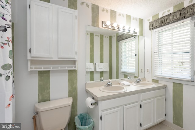 bathroom with a textured ceiling, toilet, and double vanity