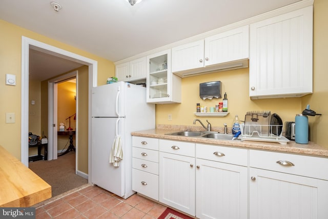 kitchen featuring a sink, freestanding refrigerator, light countertops, glass insert cabinets, and white cabinets