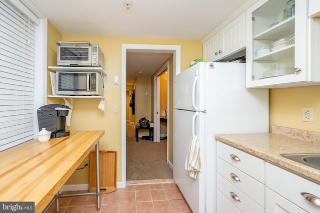 kitchen with stainless steel microwave, white cabinetry, light tile patterned floors, glass insert cabinets, and freestanding refrigerator