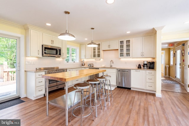 kitchen featuring appliances with stainless steel finishes, butcher block counters, decorative backsplash, light wood-style flooring, and crown molding