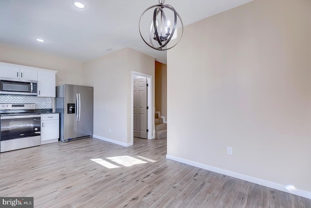 kitchen featuring backsplash, stainless steel appliances, white cabinets, decorative light fixtures, and light wood-type flooring