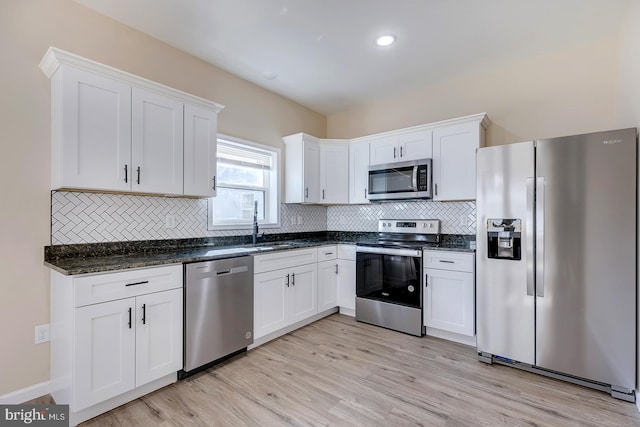 kitchen with dark stone countertops, appliances with stainless steel finishes, light wood-type flooring, and white cabinets