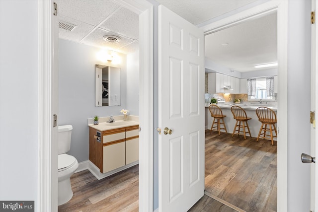 bathroom with vanity, hardwood / wood-style flooring, toilet, and a drop ceiling