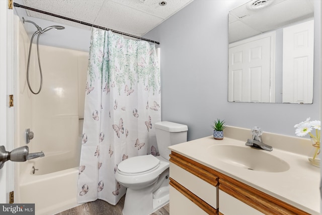 full bathroom featuring wood-type flooring, vanity, shower / tub combo, toilet, and a drop ceiling