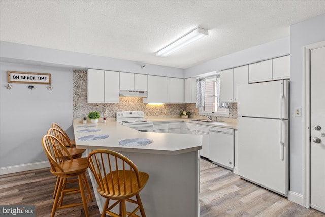 kitchen with white appliances, a kitchen breakfast bar, kitchen peninsula, and white cabinets