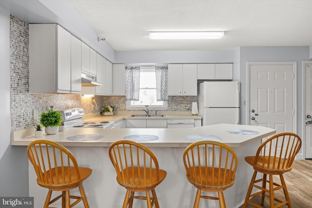 kitchen with sink, white appliances, a breakfast bar, and kitchen peninsula