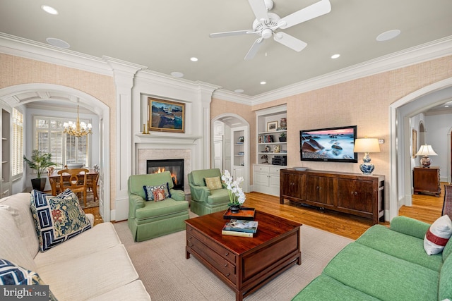 living room featuring crown molding, ceiling fan with notable chandelier, light wood-type flooring, and built in shelves