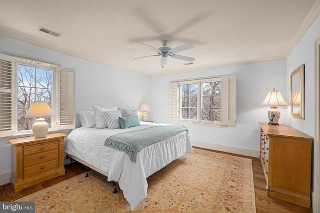 bedroom featuring multiple windows, light hardwood / wood-style flooring, ornamental molding, and ceiling fan