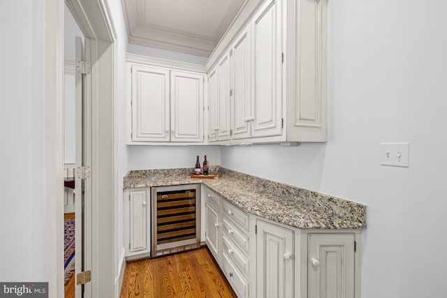 bar with light hardwood / wood-style flooring, wine cooler, light stone counters, ornamental molding, and white cabinets