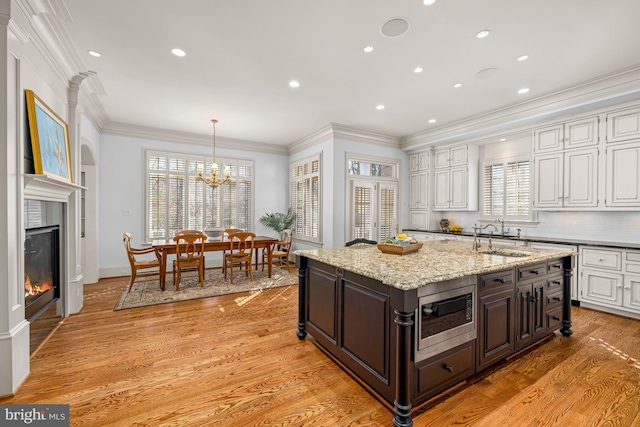 kitchen with stainless steel microwave, hanging light fixtures, dark brown cabinets, and white cabinets