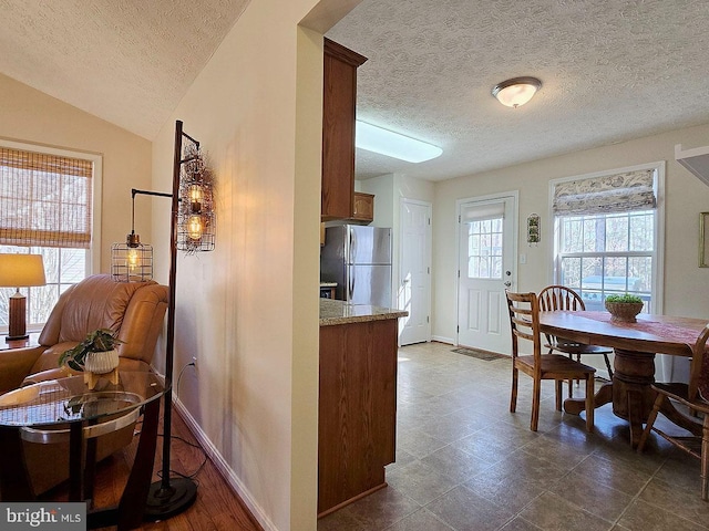 kitchen with lofted ceiling, light stone counters, a textured ceiling, and stainless steel refrigerator