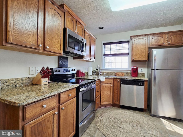 kitchen with light stone countertops, appliances with stainless steel finishes, sink, and a textured ceiling