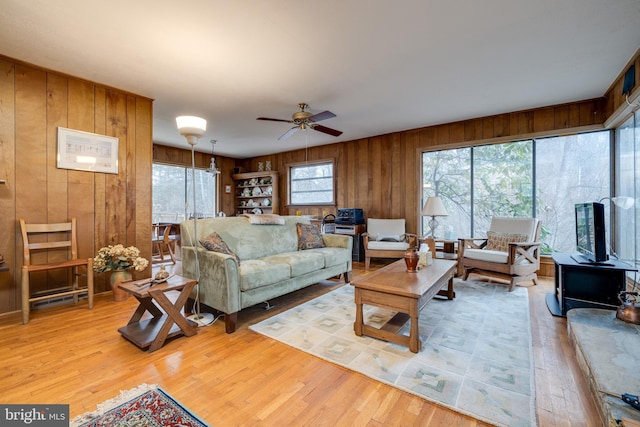 living room with a wood stove, wood walls, ceiling fan, and light hardwood / wood-style flooring