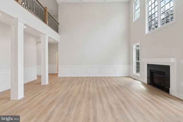 unfurnished living room with ornate columns, wood finished floors, and a glass covered fireplace