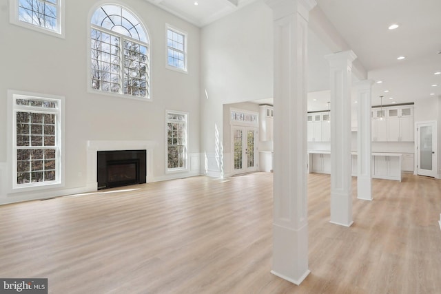 unfurnished living room featuring light wood finished floors, decorative columns, a glass covered fireplace, a towering ceiling, and recessed lighting