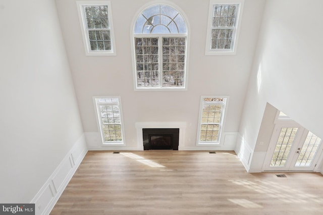 unfurnished living room with wood finished floors, a glass covered fireplace, a towering ceiling, and a decorative wall