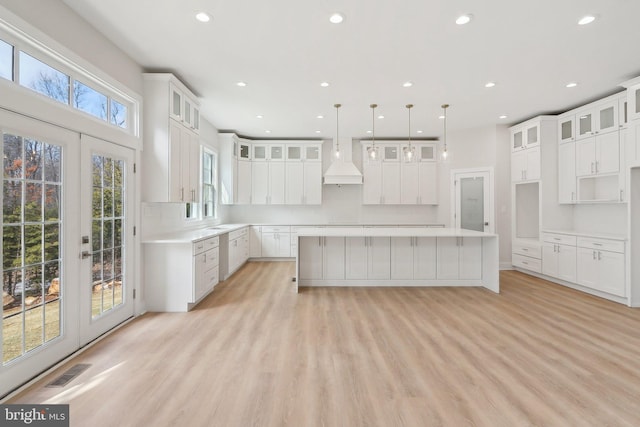 kitchen featuring a center island, recessed lighting, light wood-style floors, glass insert cabinets, and premium range hood