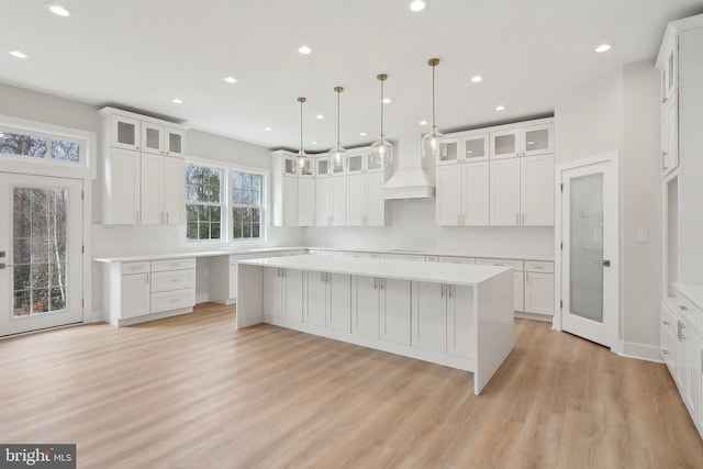 kitchen with premium range hood, a kitchen island, white cabinetry, and light wood-style floors