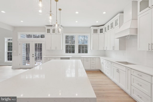 kitchen featuring light wood-style floors, white cabinets, french doors, stovetop, and custom range hood