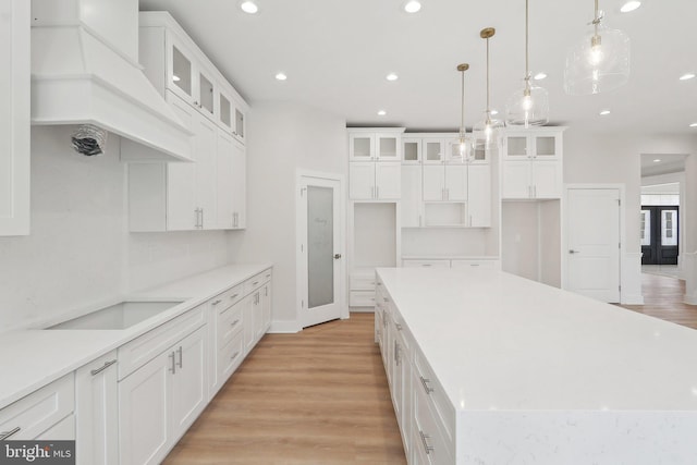 kitchen featuring white cabinets, premium range hood, a kitchen island, and light wood-style flooring