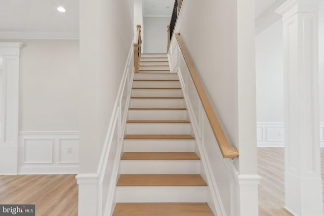 stairway with crown molding, recessed lighting, wood finished floors, and a decorative wall