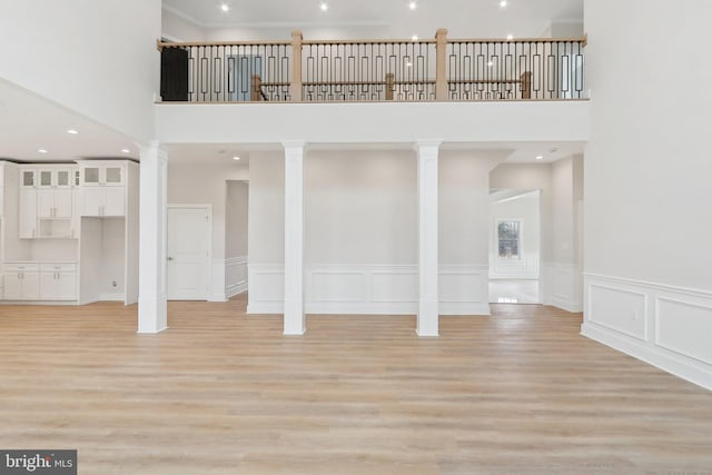 unfurnished living room with light wood-style floors, a decorative wall, a towering ceiling, and ornate columns