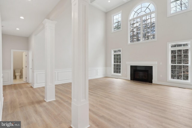 unfurnished living room with wainscoting, light wood-style flooring, ornate columns, a fireplace, and a decorative wall