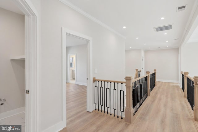 hall with visible vents, light wood finished floors, ornamental molding, and an upstairs landing