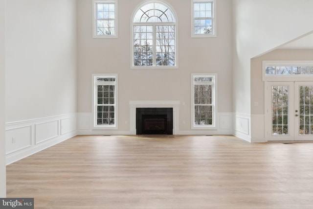 unfurnished living room featuring a towering ceiling, a fireplace with flush hearth, wood finished floors, and french doors