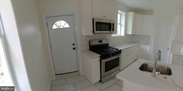 kitchen with sink, white cabinetry, tasteful backsplash, light tile patterned floors, and stainless steel appliances