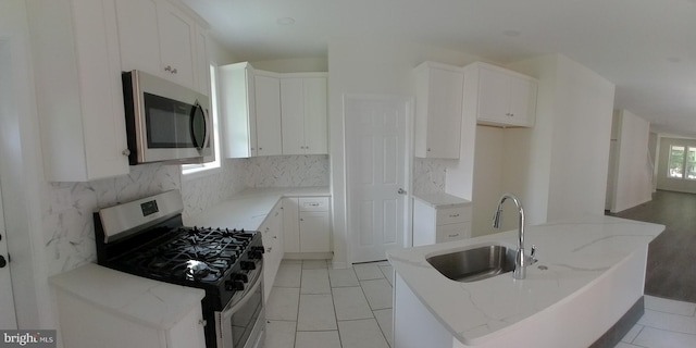 kitchen with sink, white cabinets, backsplash, stainless steel appliances, and light stone countertops