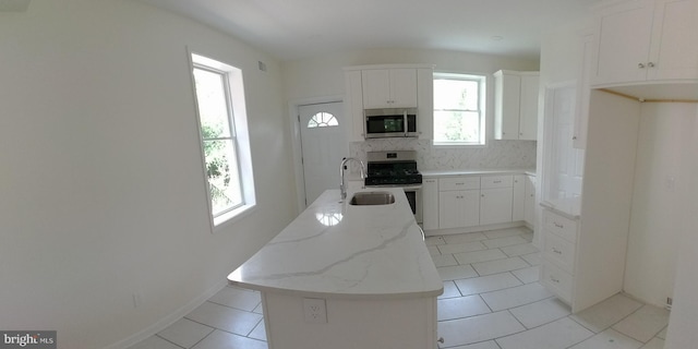 kitchen with appliances with stainless steel finishes, light stone countertops, white cabinets, a kitchen island, and decorative backsplash