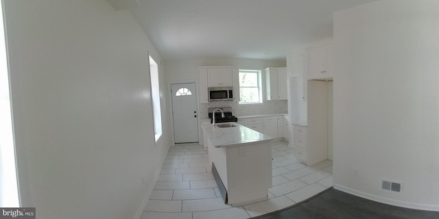 kitchen with sink, light tile patterned floors, white cabinetry, backsplash, and a kitchen island