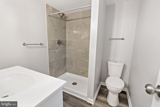 bathroom featuring hardwood / wood-style flooring, vanity, a tile shower, and toilet