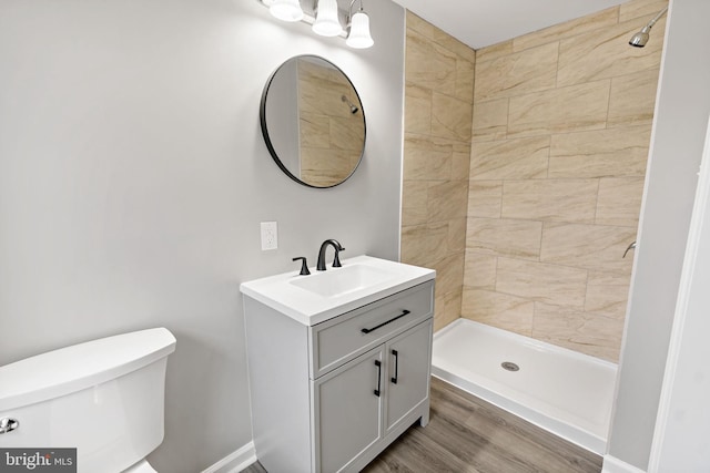 bathroom with wood-type flooring, tiled shower, vanity, and toilet